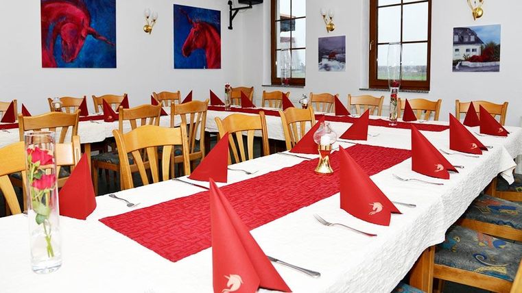Ein schön gedeckter Tisch in einem Restaurant mit roten Servietten und einer weißen Tischdecke. Die Wände sind mit Bildern von Pferden dekoriert.