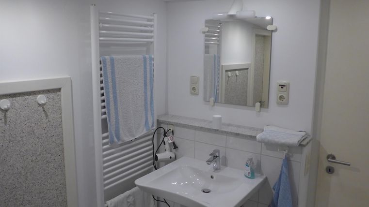 Ein modernes Badezimmer mit einem Waschbecken und einem Spiegel. Handtücher hängen an der Wand und eine angenehme Beleuchtung sorgt für eine einladende Atmosphäre.