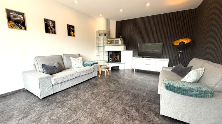 Ein modernes Wohnzimmer mit zwei hellen Sofas und einem Fernseher. Die Wände sind teilweise dunkel gestaltet und mit Bildern dekoriert.