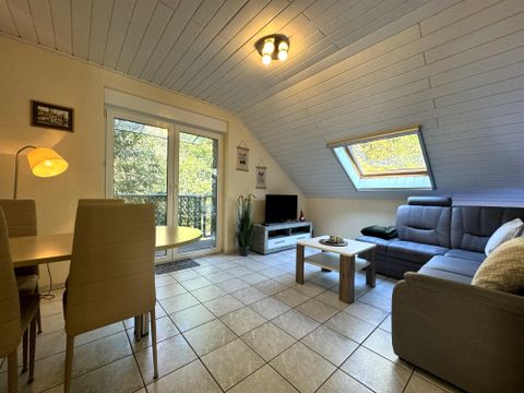 Helles Wohnzimmer mit einem bequemen Sofa und einem Esstisch. Große Fenster sorgen für viel Tageslicht und eine angenehme Atmosphäre.