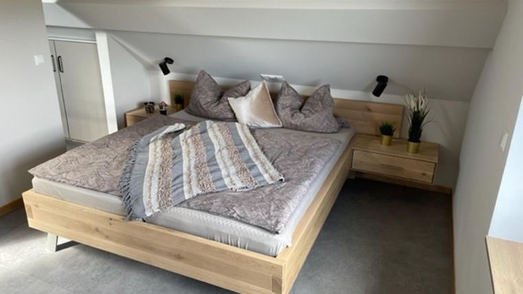 Ein modernes Schlafzimmer mit einem großen Holzbett und gemütlichen Kissen. Die Wände sind hell gestrichen und der Boden ist mit Teppich ausgelegt.