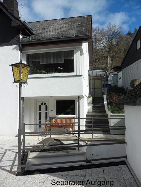 Ein modernes Haus mit einem separaten Eingang und einer Treppe. Vor dem Haus befindet sich eine kleine Sitzgelegenheit.