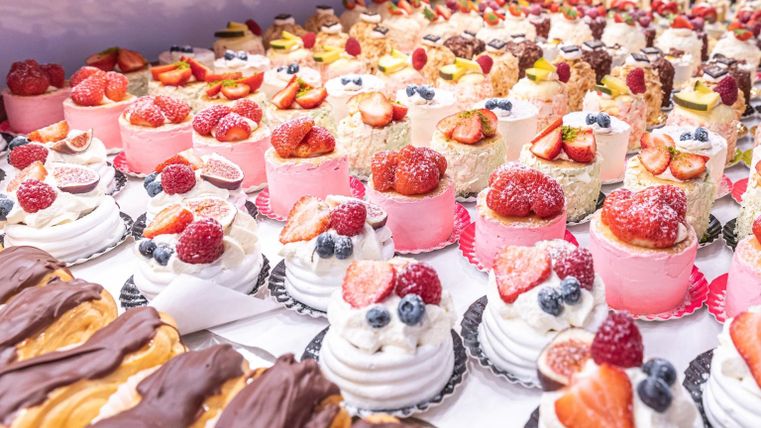 Eine bunte Auswahl an kleinen Torten und Desserts, garniert mit frischen Früchten. Die Leckereien strahlen in verschiedenen Farben und laden zum Probieren ein.
