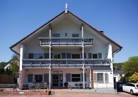 Ein charmantes Hotelgebäude im Alpenstil mit zwei Balkonen. Die Fassade ist weiß, und der Himmel ist klar und blau.