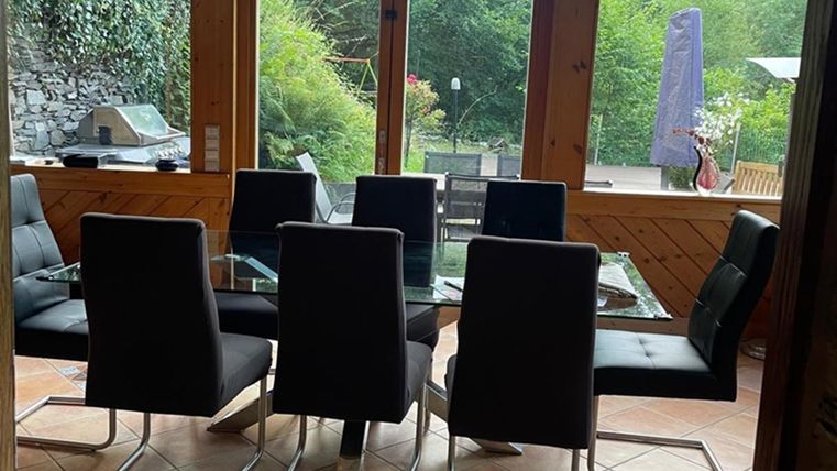 Ein moderner Essbereich mit einem Glastisch und schwarzen Stühlen. Große Fenster bieten einen Blick auf die grüne Umgebung.