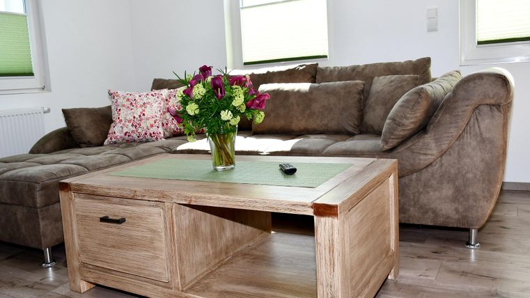 Ein gemütliches Wohnzimmer mit einem braunen Sofa und einem Holztisch. Auf dem Tisch steht ein Blumenstrauß in einer Vase.