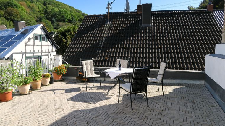 Eine helle Terrasse mit einem Tisch und Stühlen. Umgeben von Pflanzen und einer schönen Aussicht auf die umliegenden Hügel.