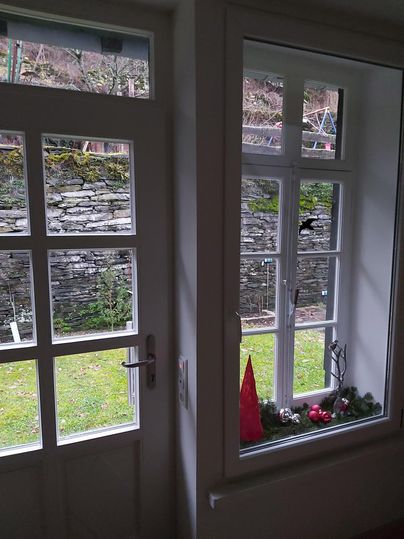 Ein Fenster mit Blick auf einen grünen Garten. Auf der Fensterbank sind dekorative Weihnachtsartikel wie ein roter Tent und kleine Kugeln.