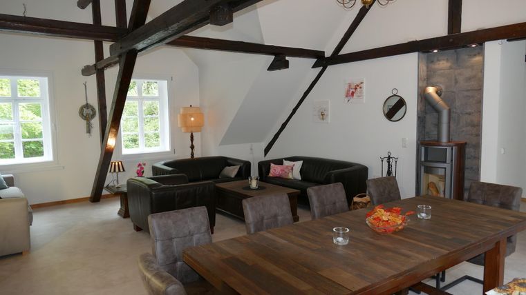 Ein modernes Wohnzimmer mit Holzbalken und einer gemütlichen Sitzecke. Ein großer Tisch lädt zum Essen und Beisammensein ein.