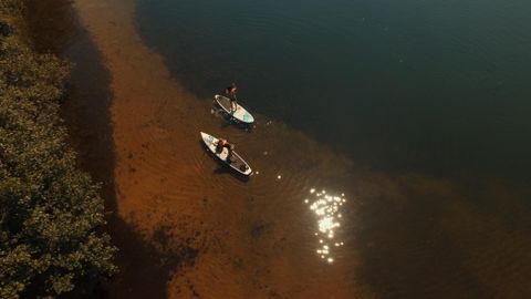 Zwei Personen paddeln in Kanus auf einem ruhigen Gewässer. Der Boden des Gewässers ist sichtbar und es funkelt im Sonnenlicht.