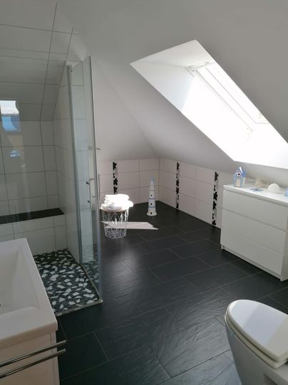 Ein modernes Badezimmer mit Dusche, Badewanne und minimalistischem Design. Große Dachfenster sorgen für viel Tageslicht.