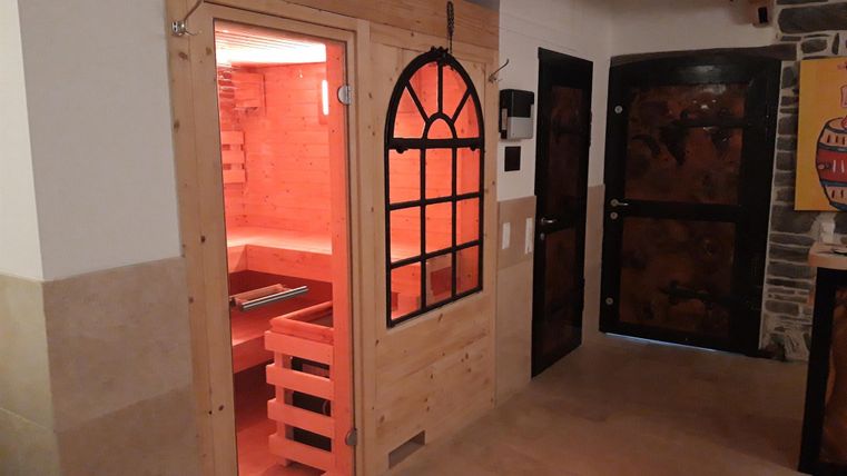 Ein gemütlicher Raum mit einer Sauna und dunklen Türen. Die Sauna ist aus Holz und beleuchtet in einem warmen, roten Licht.