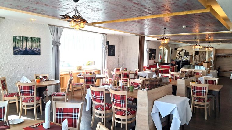 Eine elegante Restaurantumgebung mit Tischdecken und gedeckten Tischen. Im Vordergrund steht ein auffälliger Weinflaschenständer.