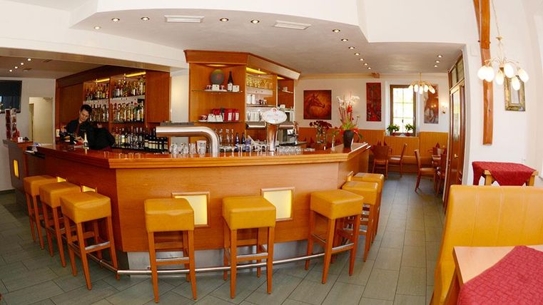 Eine gemütliche Bar mit Holzinterieur und bunten Stühlen. Im Hintergrund sind Tische und eine freundliche Atmosphäre zu sehen.