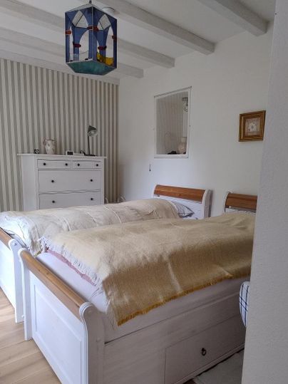 Ein gemütliches Schlafzimmer mit zwei Betten und einer hellen Wandgestaltung. Eine bunte Deckenlampe und ein Schrank runden das Bild ab.