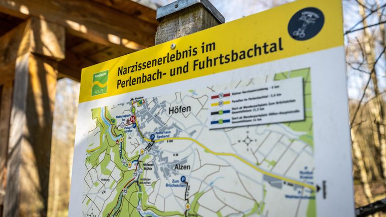 Ein Wegweiser mit einer Karte des Narzissenerlebnisses im Perlenbach- und Fuhrtbachtal. Die Karte zeigt verschiedene Wege und Orte in der Umgebung.