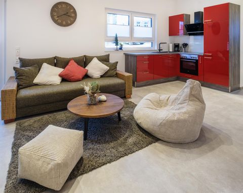 Eine moderne Wohnküche mit einem gemütlichen Sofa und einem runden Tisch. Die roten Küchenschränke setzen einen schönen Akzent im Raum.
