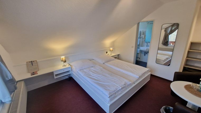 Ein gemütliches Schlafzimmer mit zwei Einzelbetten und warmem Licht. Im Hintergrund ist ein moderner Badebereich sichtbar.