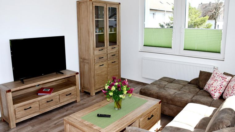 Ein modernes Wohnzimmer mit einem Fernseher, einer eleganten Holzkommode und einem bequemen Sofa. Auf dem Tisch steht eine Vase mit bunten Blumen.