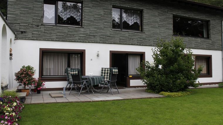 Ein modernes Haus mit zwei Etagen und großen Fenstern. Draußen befindet sich eine Terrasse mit Gartenmöbeln und ein gepflegter Rasen.