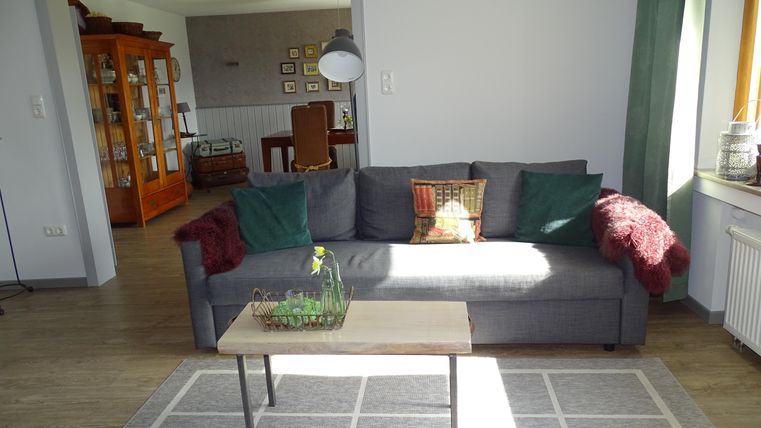 Ein gemütliches Wohnzimmer mit einem grauen Sofa und einem Holztisch. Der Raum ist hell erleuchtet und hat eine einladende Atmosphäre.