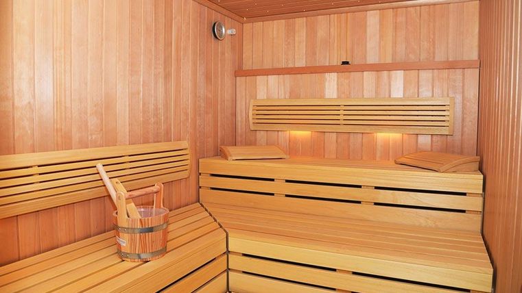 Eine moderne Sauna aus Holz mit gemütlichen Bänken und einer rustikalen Holzwanne. Sanftes Licht sorgt für eine entspannte Atmosphäre.