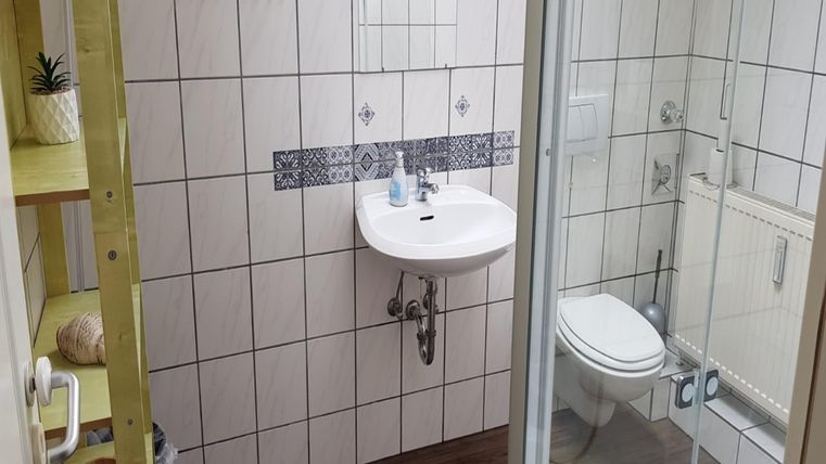 Ein modernes Badezimmer mit einem Waschbecken, einer Dusche und einer Toilette. Die Wände sind mit hellen Fliesen und dekorativen Mustern gestaltet.