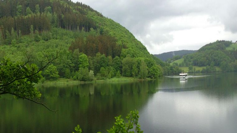 Eine ruhige Landschaft mit einem See und grünen Hügeln. Ein Boot fährt gemächlich auf dem Wasser.