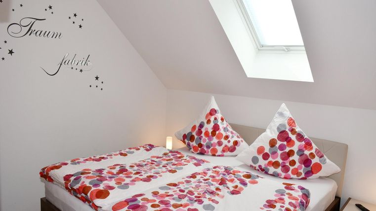Ein gemütliches Schlafzimmer mit einem Doppelbett und bunten Kissen. An der Wand steht der Schriftzug "Traumfabrik".