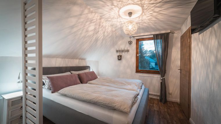 Ein modernes Schlafzimmer mit einem großen Bett und gemütlicher Bettwäsche. Das Fenster lässt Tageslicht hinein und schafft eine einladende Atmosphäre.