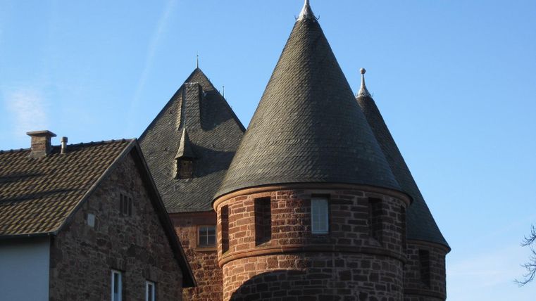 Ein historisches Gebäude mit markanten Türmen und einem klaren, blauen Himmel. Die Architektur zeigt eine Kombination aus Steinmauerwerk und spitzen Dächern.