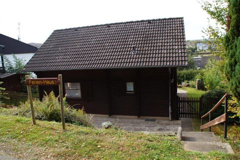 Ein rustikales Ferienhaus mit brauner Holzfassade. Es steht in einer grünen Umgebung mit einem kleinen Garten und einem Weg zur Haustür.
