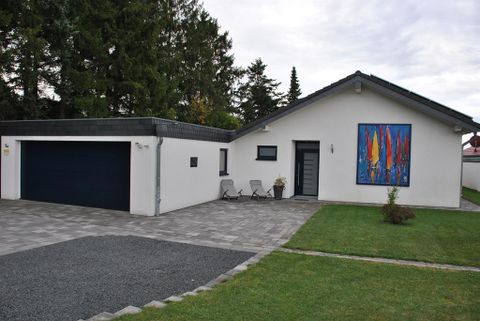 Ein modernes Haus mit einem großen Garagentor und buntem Kunstwerk an der Wand. Im Vordergrund befindet sich ein gepflegter Garten mit Sitzecke.