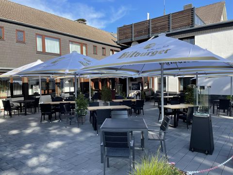 Eine einladende Terrasse mit Tischen und Stühlen unter großen Sonnenschirmen. Im Hintergrund ist ein Gebäude zu sehen, das eine entspannte Atmosphäre schafft.