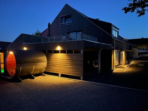Ein modernes Gebäude bei Nacht, beleuchtet von warmen Lichtern. Auf der linken Seite steht eine charakteristische Sauna mit runder Form.