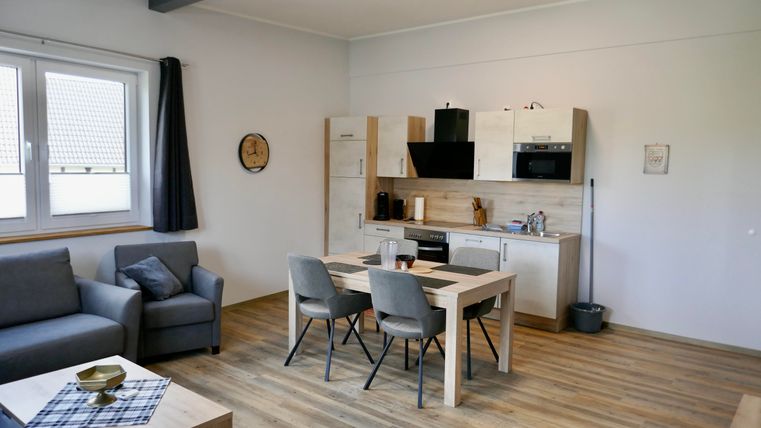 Ein modernes Wohnzimmer mit einer offenen Küche. Es gibt einen Esstisch mit Stühlen und eine gemütliche Couch.