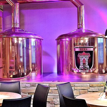Zwei große Kupferkessel für die Bierbrauerei stehen vor einer lila beleuchteten Wand. Der Kessel auf der linken Seite trägt das Logo einer Brauerei.