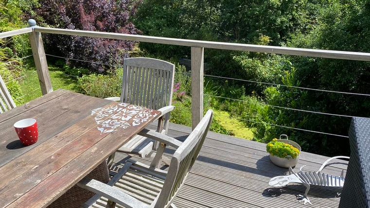 Ein gemütlicher Balkon mit einem Holztisch und Stühlen. Im Hintergrund sieht man üppiges Grün und eine schöne Pflanzenlandschaft.