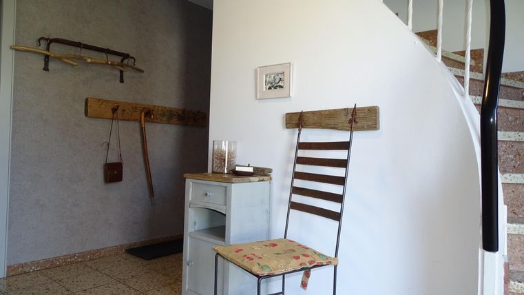 Eine gemütliche Diele mit einem Stuhl und einer kleinen Kommode. An der Wand hängen dekorative Gegenstände und ein Kunstwerk.