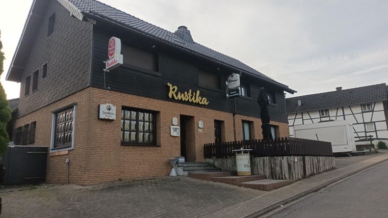 Ein traditionelles restaurant in einem zweistöckigen Gebäude mit einem einladenden Außenbereich. Die Fassade ist in einem Mix aus Ziegelstein und dunklem Putz gehalten.