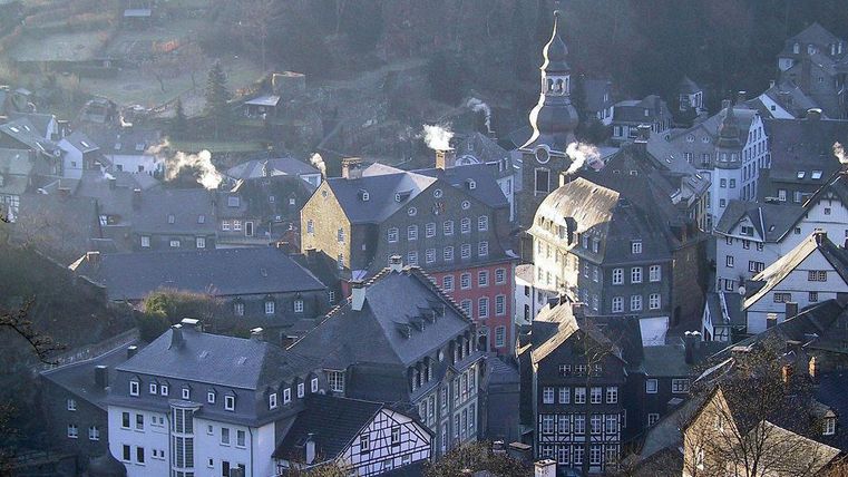 Eine malerische Stadt mit historischen Gebäuden und schmalen Gassen. Der Rauch aus den Schornsteinen deutet auf eine gemütliche Atmosphäre hin.