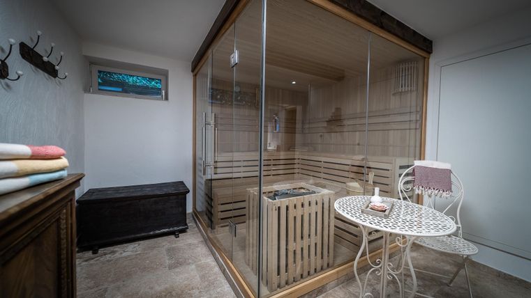 Ein moderner Saunabereich mit großen Glaswänden. Neben der Sauna steht ein kleiner Tisch und eine gemütliche Sitzgelegenheit.