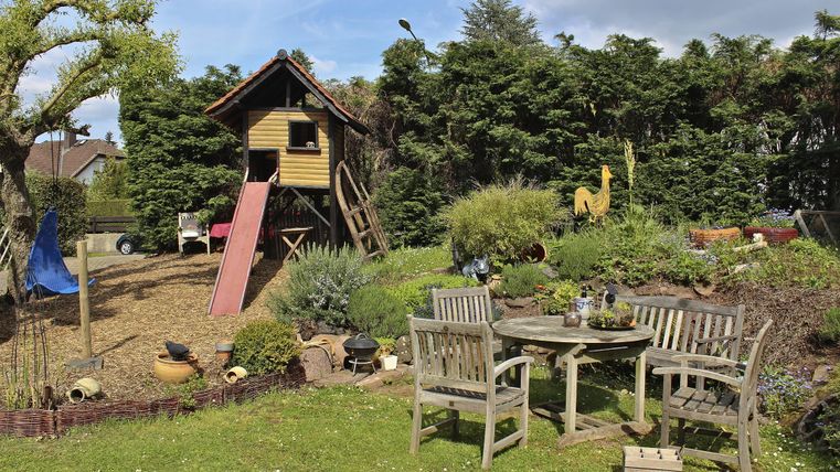 Ein schöner Garten mit einem Spielhaus und einer Rutsche. Gemütliche Möbel laden zum Entspannen ein.