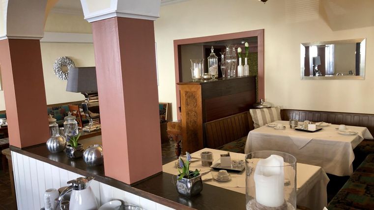 Ein elegantes Restaurant mit hellen Wänden und gemütlichen Tischen. Auf der Theke stehen Getränke und Dekorationen.