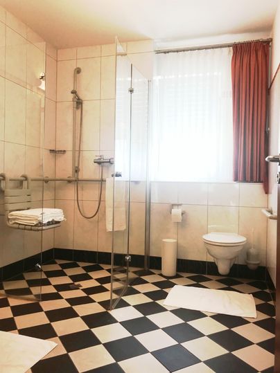 Ein modernes Badezimmer mit Fliesenboden in Schwarz-Weiß. Es verfügt über eine begehbare Dusche, Handtücher und eine große Fensterfront.