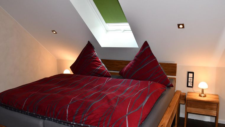 Ein gemütliches Schlafzimmer mit einem großen Doppelbett und roten Kissen. Das Zimmer hat ein Dachfenster und eine Nachttischlampe.