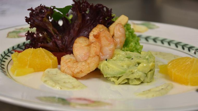 Ein ansprechend angerichteter Teller mit Shrimps, Salatblättern und cremigem Avocado-Dip. Dazu sind frische Orangenstücke arrangiert.