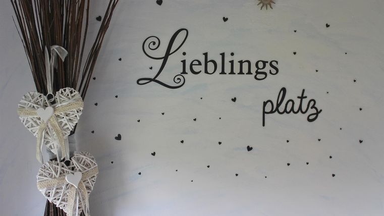 Ein dekorativer Wandbereich mit der Aufschrift "Lieblingsplatz". Neben der Wand stehen zwei herzförmige Dekorationen und einige Zweige.