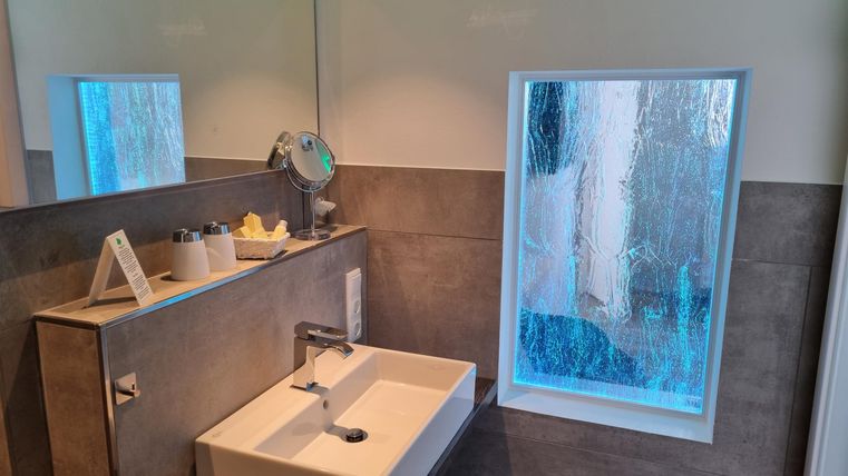 Ein modernes Badezimmer mit einem schlichten Waschbecken und einem großen Fenster. Der Raum wirkt hell und einladend.