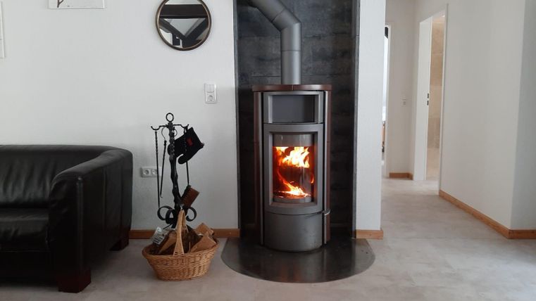 Ein moderner Kamin steht in einem hellen, gemütlichen Raum. Der Raum hat eine entspannende Atmosphäre mit einem bequemen Sofa und einem Korbwarenständer.